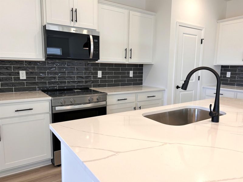 Kitchen featuring white cabinets, stainless steel appliances, light stone countertops, and tasteful backsplash