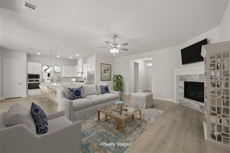 The open living room with a premium fireplace, ceiling fan, and light wood LVP flooring is easy to maintain.