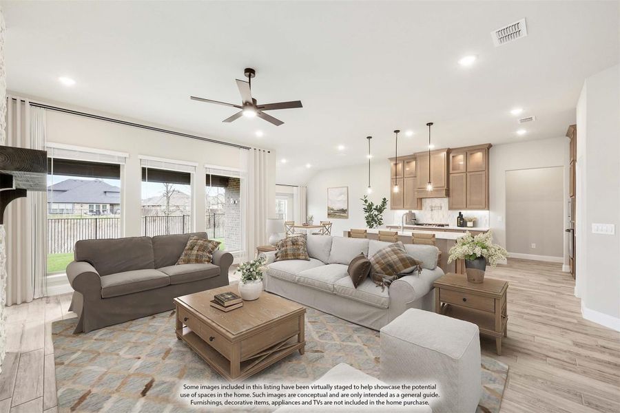 Open-concept living room with ceiling fan and light wood floors, open to kitchen with wood cabinets and pendant lights