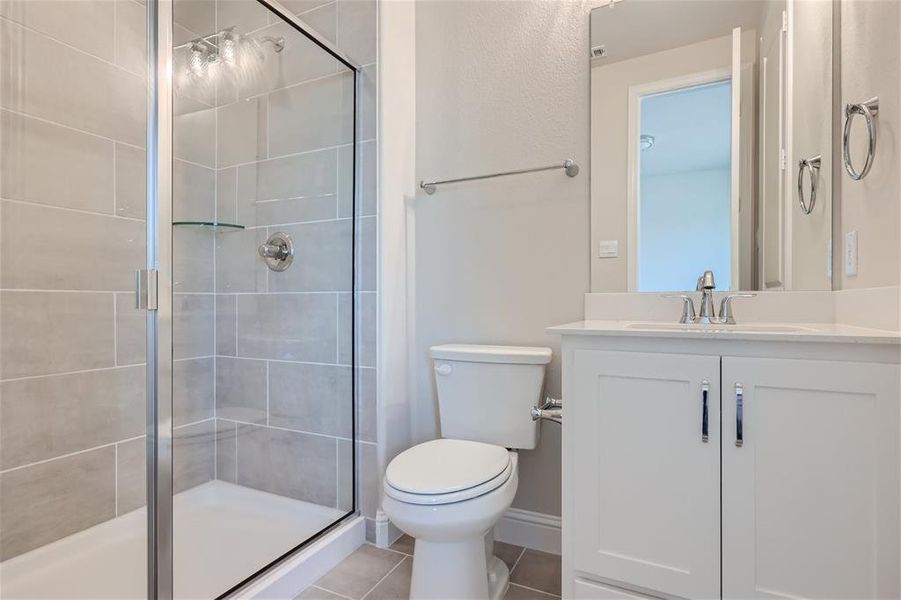 Bathroom featuring tile patterned floors, a shower with door, vanity, and toilet