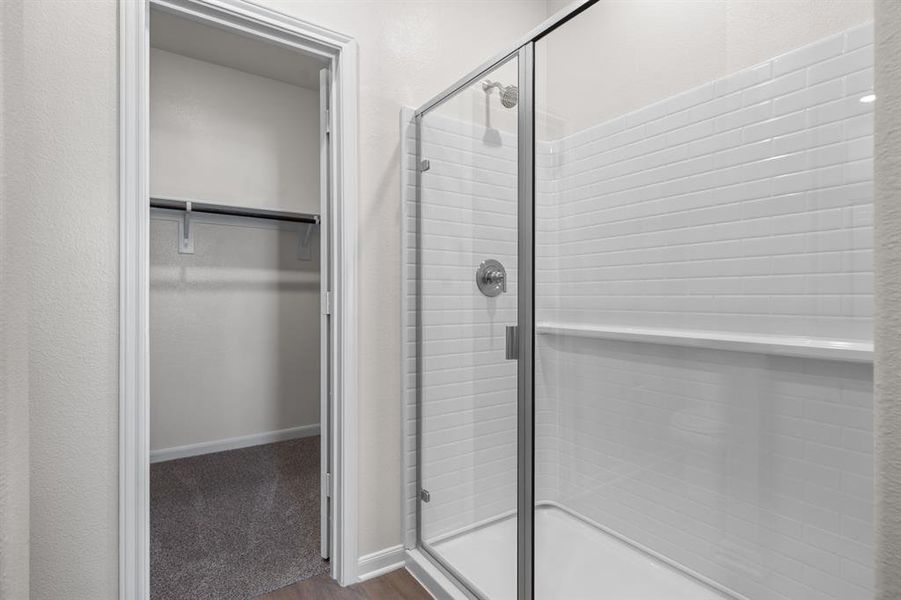 Full bathroom featuring a spacious closet, a shower stall, and dark wood-type flooring