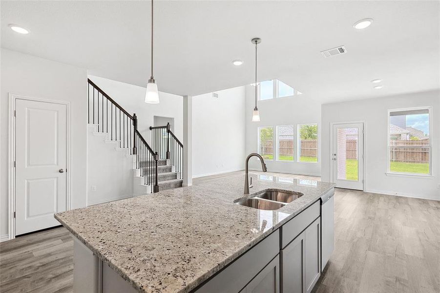 Kitchen featuring sink, a kitchen island with sink, light stone counters, and light hardwood / wood-style flooring