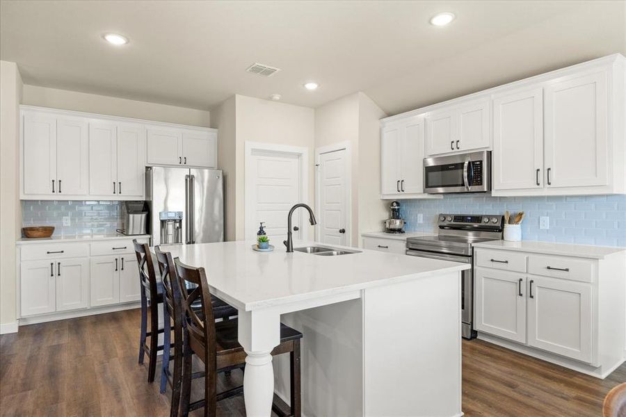 Kitchen featuring tasteful backsplash, appliances with stainless steel finishes, a breakfast bar, white cabinetry, and an island with sink