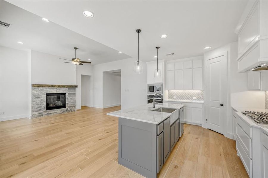 Dual tone kitchen featuring dual tone cabinets, an island with sink, a stone fireplace, light wood-type flooring, and light stone counters