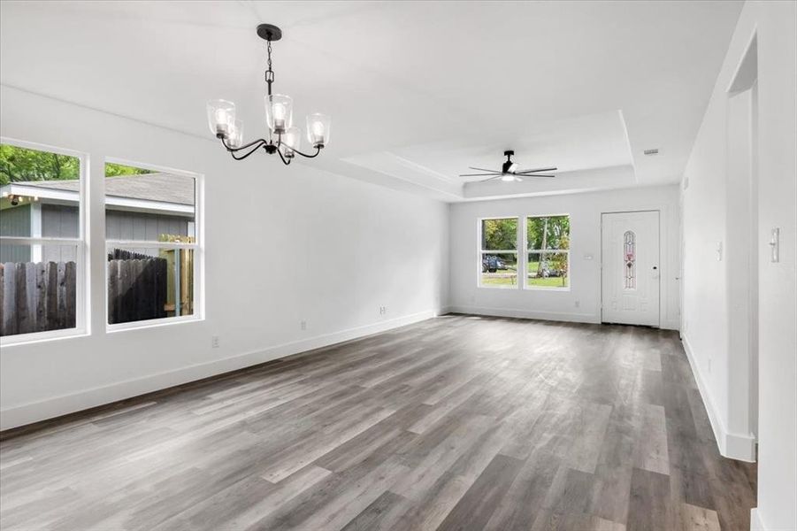 Empty room featuring ceiling fan with notable chandelier, a tray ceiling, and hardwood / wood-style flooring