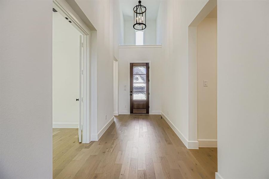 Foyer entrance featuring light wood finished floors, a chandelier, and a towering ceiling