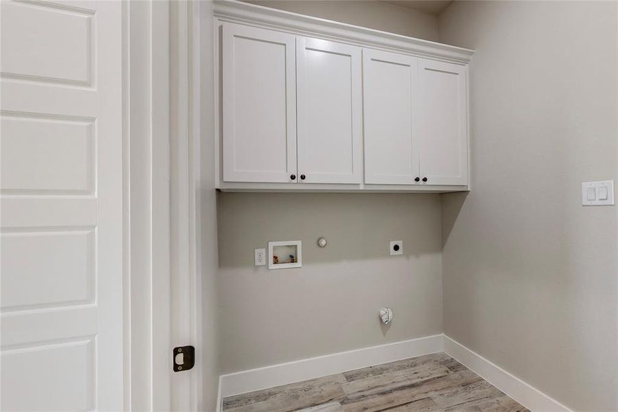 Clothes washing area with hookup for a gas dryer, electric dryer hookup, hookup for a washing machine, cabinets, and light hardwood / wood-style floors