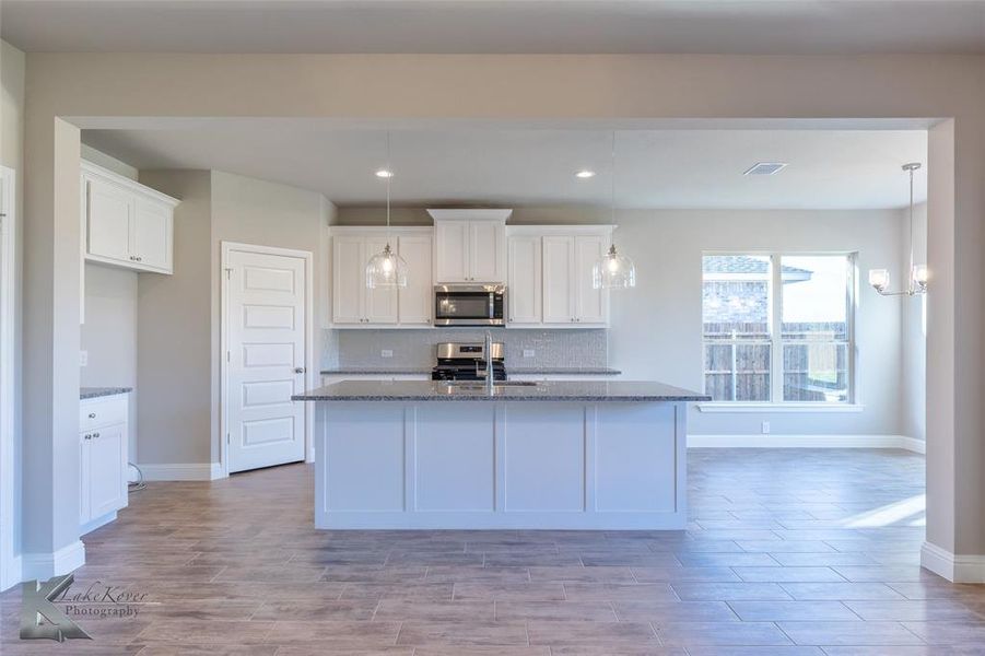 Kitchen with white cabinets, decorative backsplash, dark stone counters, an island with sink, and stainless steel appliances