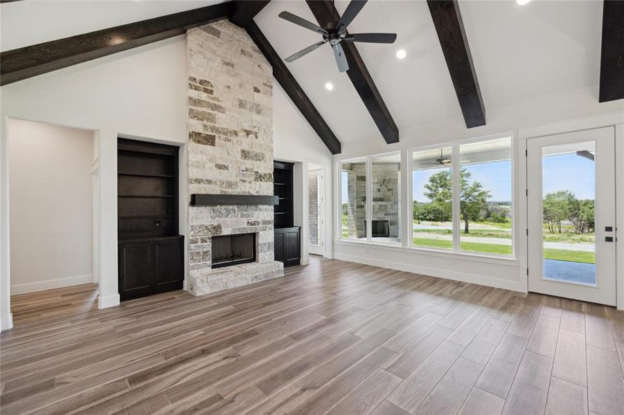 Unfurnished living room featuring a stone fireplace, beamed ceiling, ceiling fan, and hardwood / wood-style floors