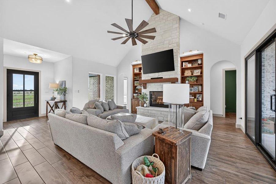 Vaulted living space featuring a stone-clad fireplace with built-in shelving, wood-finish flooring, a contemporary ceiling fan, and abundant natural light