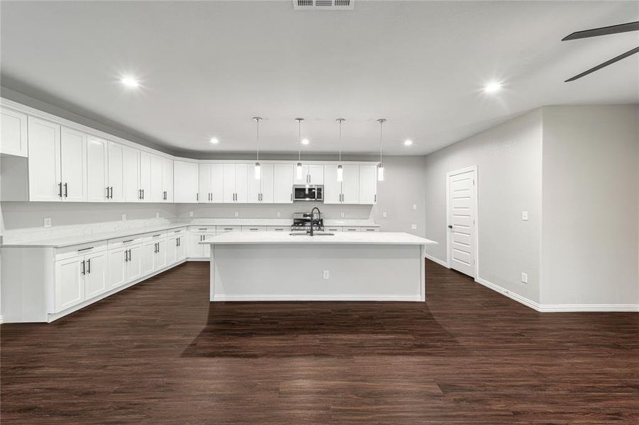 Kitchen with a center island with sink, white cabinetry, dark wood-style flooring, stainless steel appliances, and pendant lighting