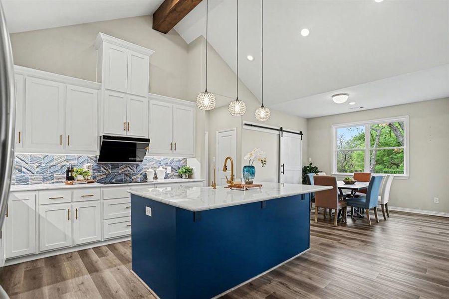 Kitchen featuring a barn door, white cabinetry, hanging light fixtures, and an island with sink