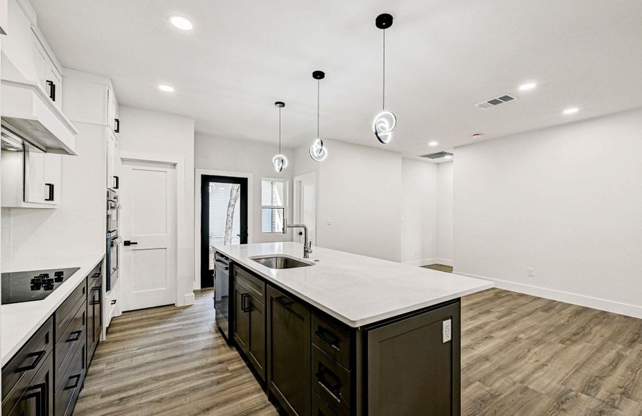 Kitchen featuring hanging light fixtures, light wood finished floors, black electric stovetop, recessed lighting, and an island with sink