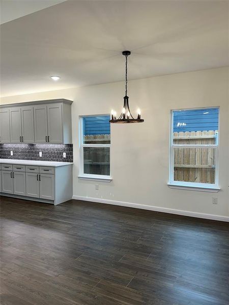 Kitchen with pendant lighting, dark wood-type flooring, gray cabinets, an inviting chandelier, and backsplash