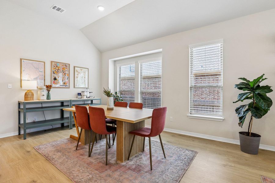 A naturally illuminated dining area features vaulted ceilings and light wood flooring.