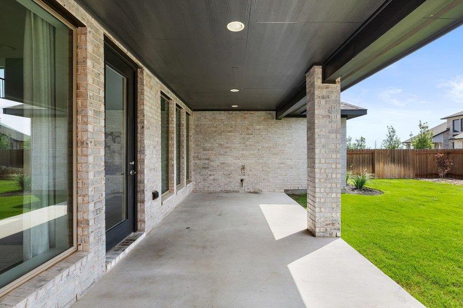 A spacious covered patio invites outdoor relaxation, overlooking a vibrant green lawn with a privacy fence.