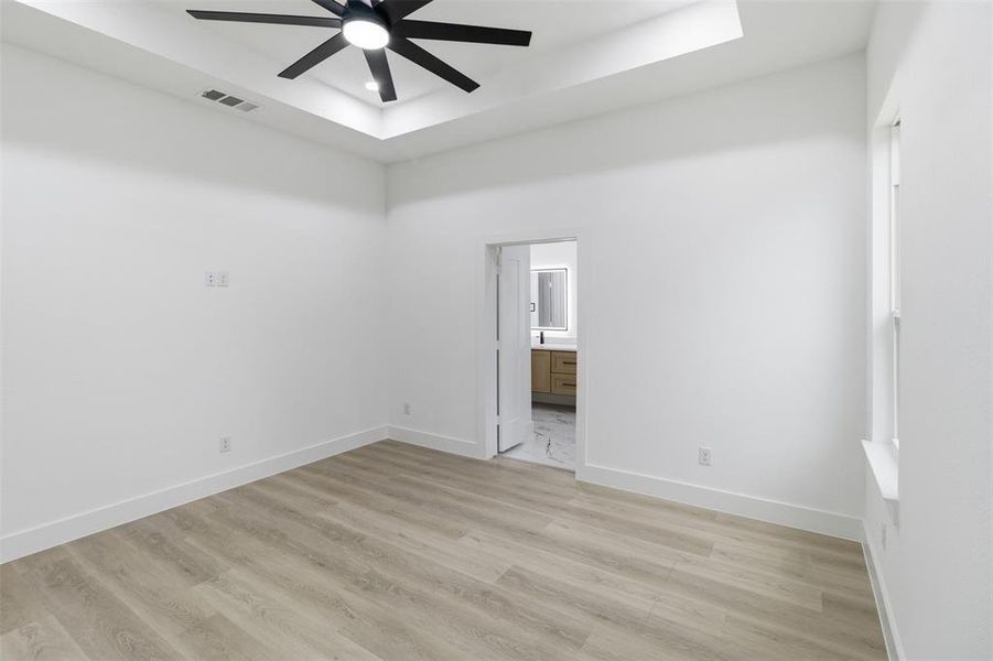 Empty room featuring a tray ceiling, light wood-style flooring, and ceiling fan