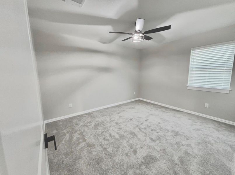 Bright and inviting upstairs bedroom with plush carpeting and a modern ceiling fan.