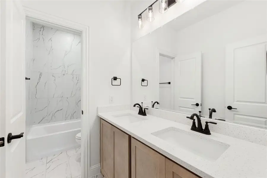 Bathroom with double sink vanity, quartz countertop, and marble-tile tub surround with black fixtures