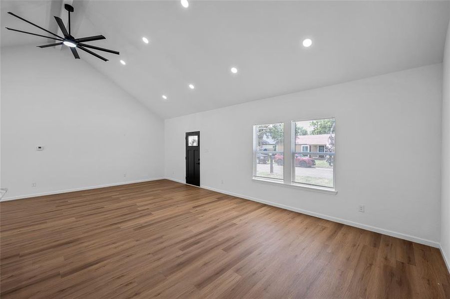 Expansive room featuring a vaulted ceiling and wood-finish flooring Expansive room featuring a vaulted ceiling and wood-finish flooring