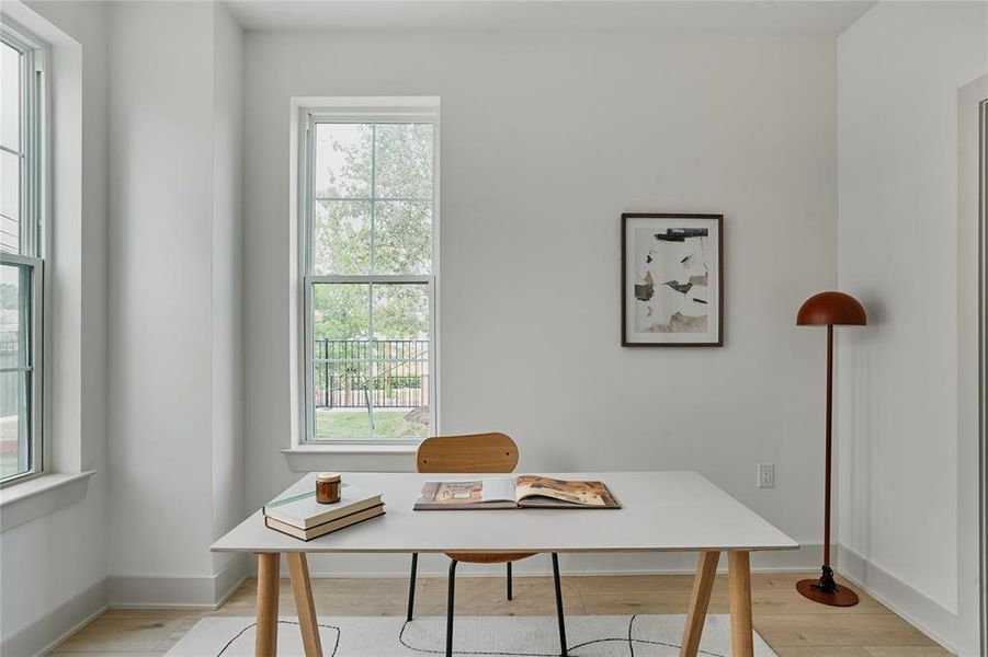 Bright room featuring two large windows with grid patterns, light wood-finish flooring, and crisp white walls