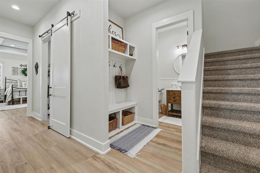 Mudroom featuring a barn door, light wood-style floors, and recessed lighting, bench and cubbies with hooks