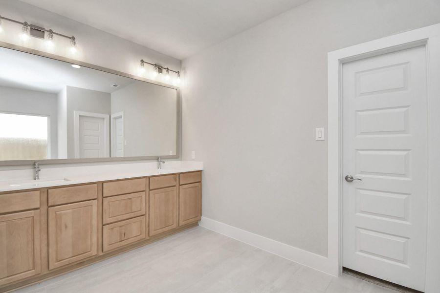 Elevate your daily routine at the elegant vanity, now equipped with double sinks, light countertops, modern hardware, and beautiful vanity lights. Sample photo of completed home with similar floor plan. Actual colors and selections may vary.