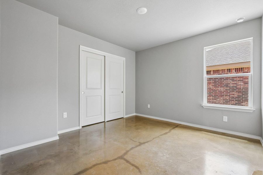 A well-lit bedroom features durable concrete flooring and a convenient sliding closet. A well-lit bedroom features durable concrete flooring and a convenient sliding closet.