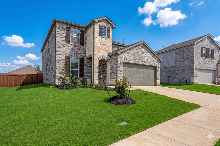 Stone and brick facade home featuring a two-car garage, arched entry, and manicured landscaping