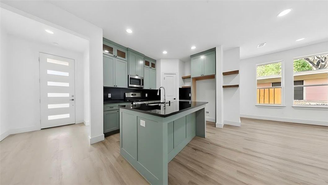 Kitchen featuring green cabinetry, glass insert cabinets, a center island with sink, stainless steel appliances, and recessed lighting