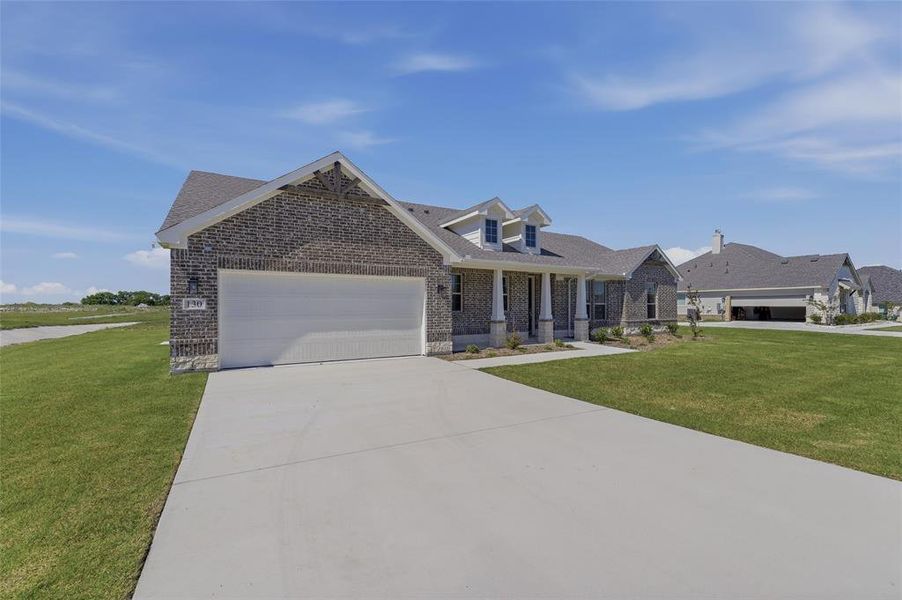 Brick exterior featuring a two-car garage, concrete driveway, and front porch with columns