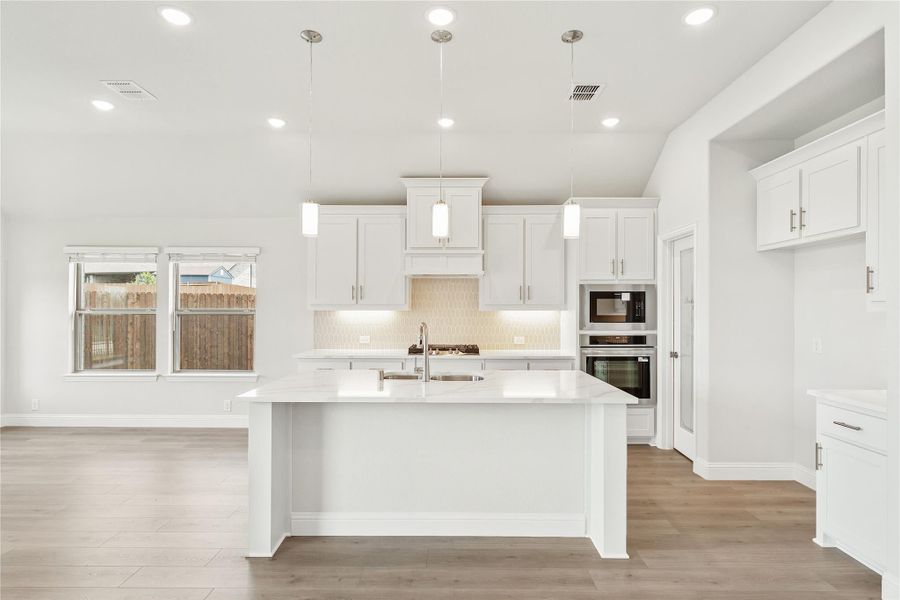 White kitchen with large center island, white cabinets, stainless steel appliances, and hardwood floors White kitchen with large center island, white cabinets, stainless steel appliances, and hardwood floors