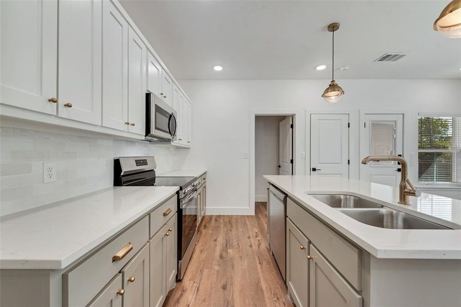 Kitchen with stainless steel appliances, gray cabinets, pendant lighting, a kitchen island with sink, and light wood finished floors Kitchen with stainless steel appliances, gray cabinets, pendant lighting, a kitchen island with sink, and light wood finished floors