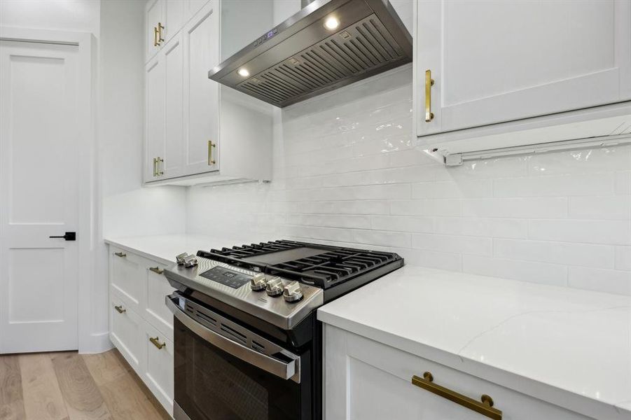 Kitchen with stainless steel gas range, wall chimney range hood, white cabinets, light stone countertops, and light hardwood / wood-style floors