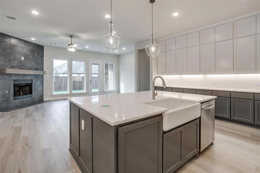 Kitchen with a center island with sink, sink, gray cabinets, light stone counters, and a tiled fireplace