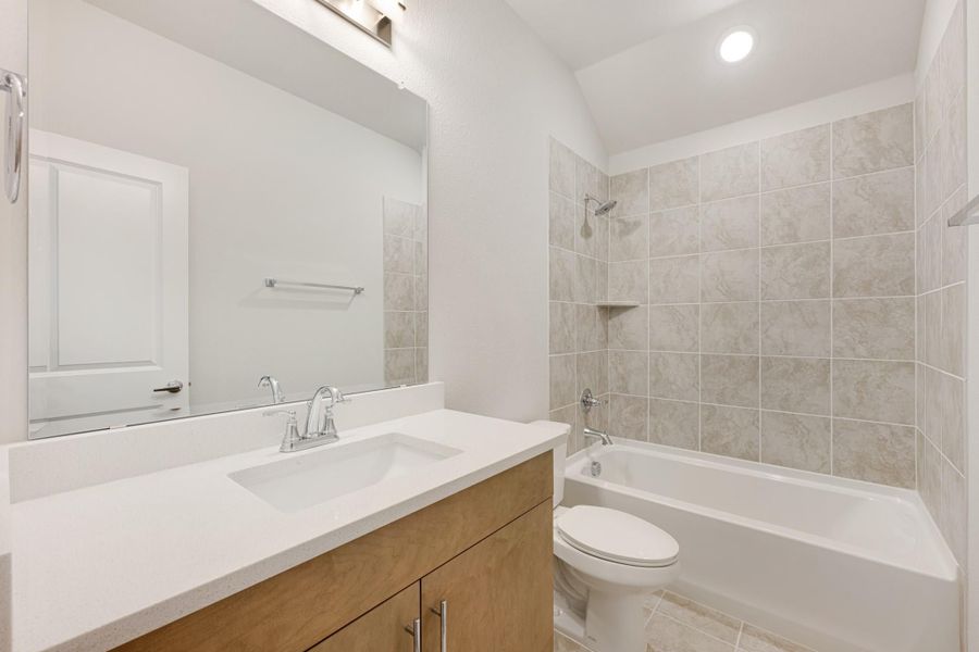 Bathroom with wood vanity, white countertop, large mirror, and tiled shower-tub combo