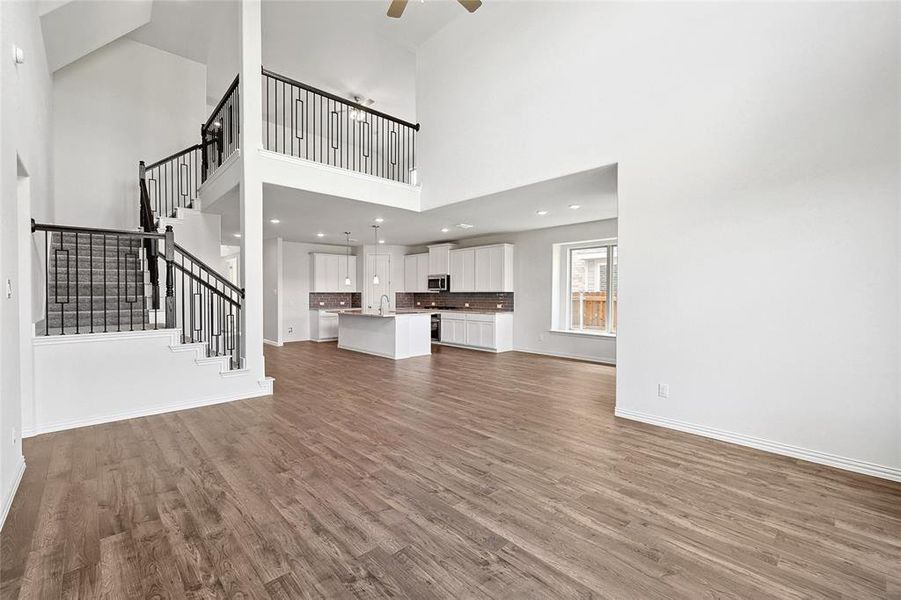 Unfurnished living room featuring sink, ceiling fan, wood-type flooring, and a towering ceiling