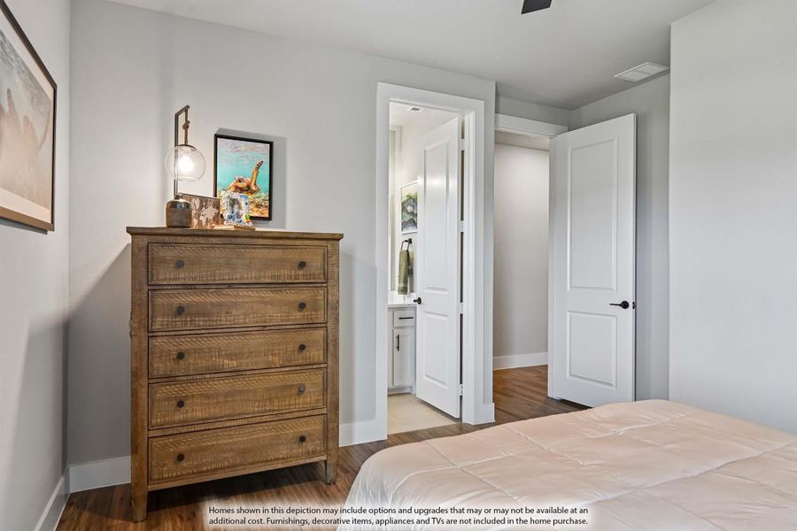 Bedroom with wood dresser, hardwood floors, and open door leading to ensuite bathroom Bedroom with wood dresser, hardwood floors, and open door leading to ensuite bathroom