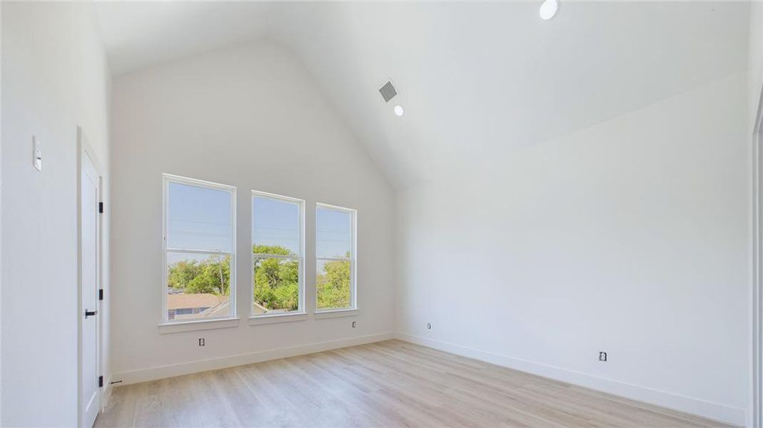 This thoughtfully designed primary bedroom features durable wood-like LVP flooring throughout. Cathedral ceilings are anchored by a stylish black ceiling fan (to be installed), while three oversized windows, paired with recessed lighting, illuminate the space.