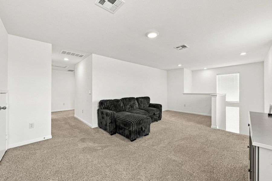 A spacious upstairs loft features soft carpeting, recessed lighting, and a view over the banister.