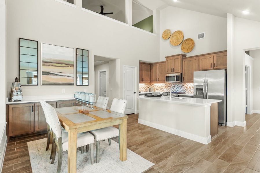 Open-concept dining area and kitchen with high ceilings, wood-look floors, and stainless steel appliances