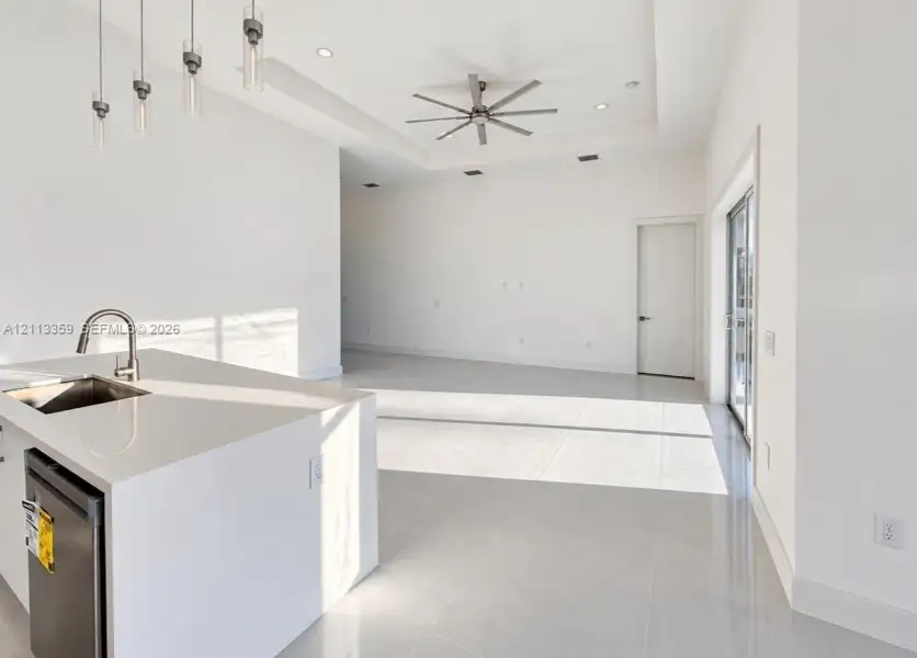 Kitchen island featuring a solid-surface countertop with an integrated undermount sink, multi-pendant lighting, recessed ceiling lighting, a tray ceiling with a multi-blade ceiling fan, and tile flooring