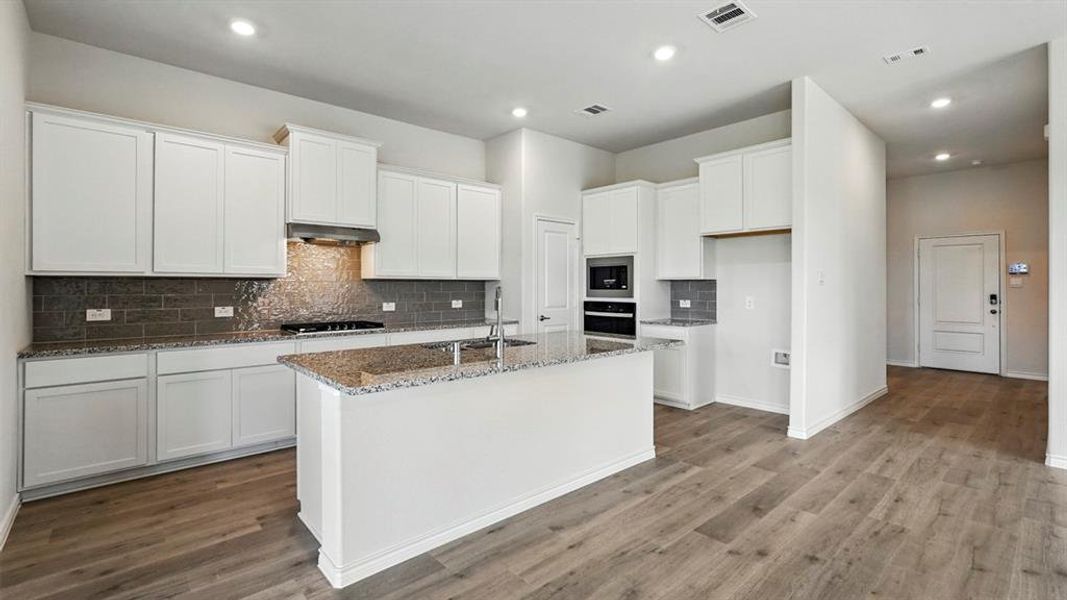 Modern kitchen featuring a central island, white cabinetry, granite countertops, and wood-finish flooring Modern kitchen featuring a central island, white cabinetry, granite countertops, and wood-finish flooring