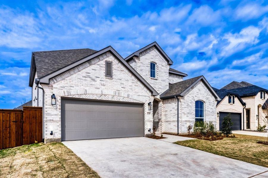 French country inspired facade featuring concrete driveway, a garage, roof with shingles, and brick siding