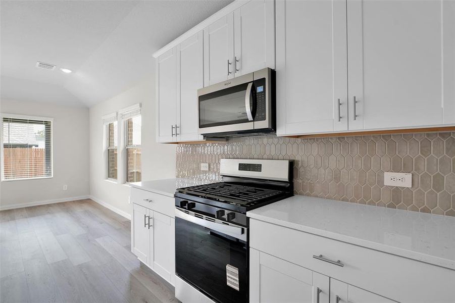 Kitchen featuring stainless steel appliances, white cabinetry, backsplash, light wood finished floors, and light stone countertops Kitchen featuring stainless steel appliances, white cabinetry, backsplash, light wood finished floors, and light stone countertops
