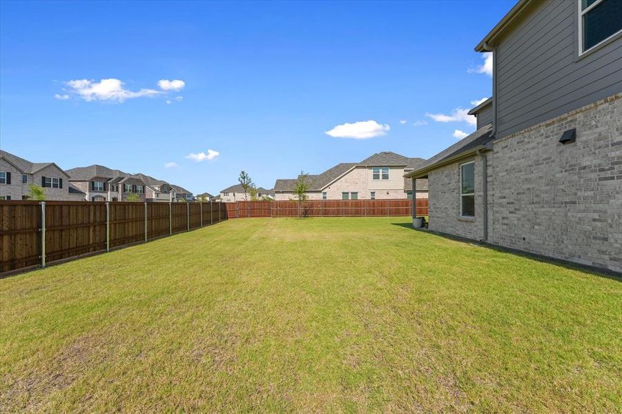 Expansive lawn area enclosed by a privacy fence, featuring a brick and siding exterior on the property