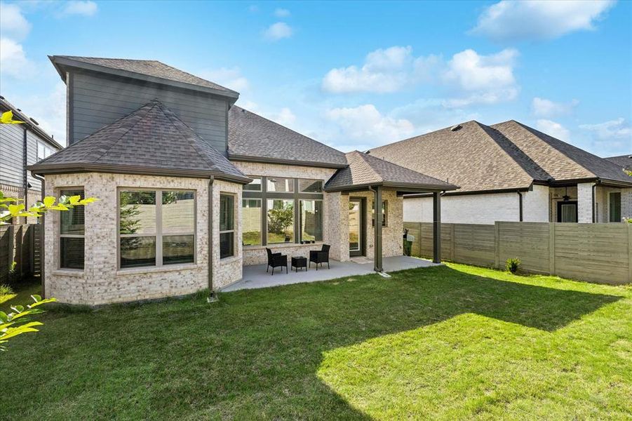 Expansive green lawn with a covered patio, brick and siding exterior, multiple windows, and a privacy fence Expansive green lawn with a covered patio, brick and siding exterior, multiple windows, and a privacy fence
