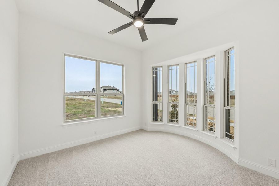 Empty bedroom with carpet, ceiling fan, and curved bay window wall overlooking neighborhood