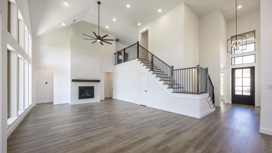 Unfurnished living room featuring dark wood-type flooring, a towering ceiling, a fireplace, a ceiling fan, and stairs Unfurnished living room featuring dark wood-type flooring, a towering ceiling, a fireplace, a ceiling fan, and stairs