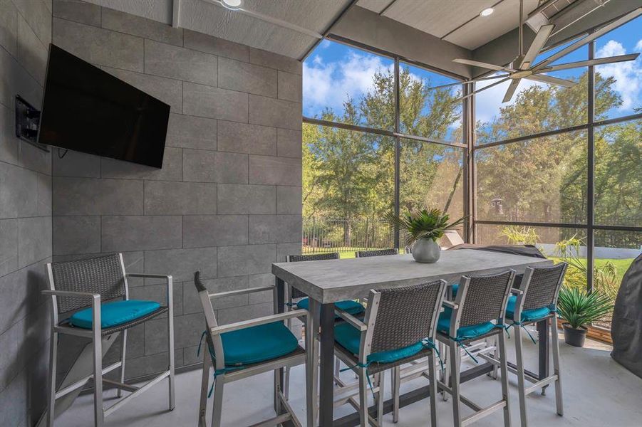Sunroom / solarium featuring outdoor dining area, a patio, a ceiling fan, and view of scattered trees